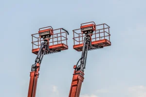 Pair of red articulated boom lift baskets raised against blue sky, showing safety railings and arms. — 100 chars