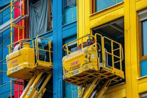 Two yellow boom lifts on building
