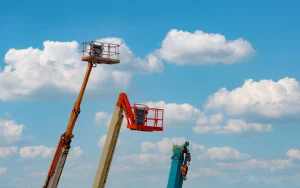 Two boom lift platforms beside a crane boom with hook, illustrating boom lift vs crane.