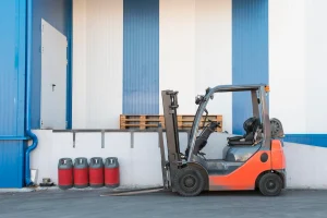 Orange forklift parked at a warehouse loading area, showing a common counterbalance forklift type used for material handling.