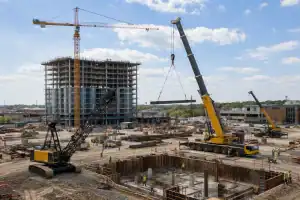 Multiple crane types operating on large construction site with tower mobile and crawler cranes