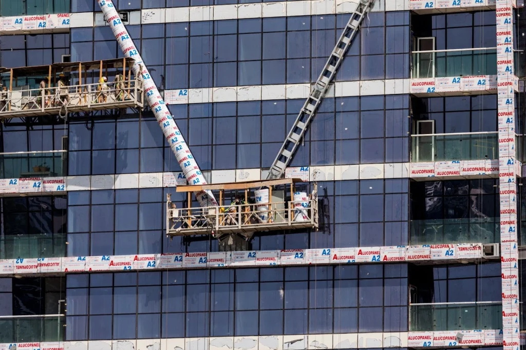 construction workers using suspended platform lift for façade installation on high-rise building
