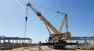 Mobile crane lifting heavy structural materials at a construction site, showing the boom, hook block, and lifting cables during industrial crane operation.