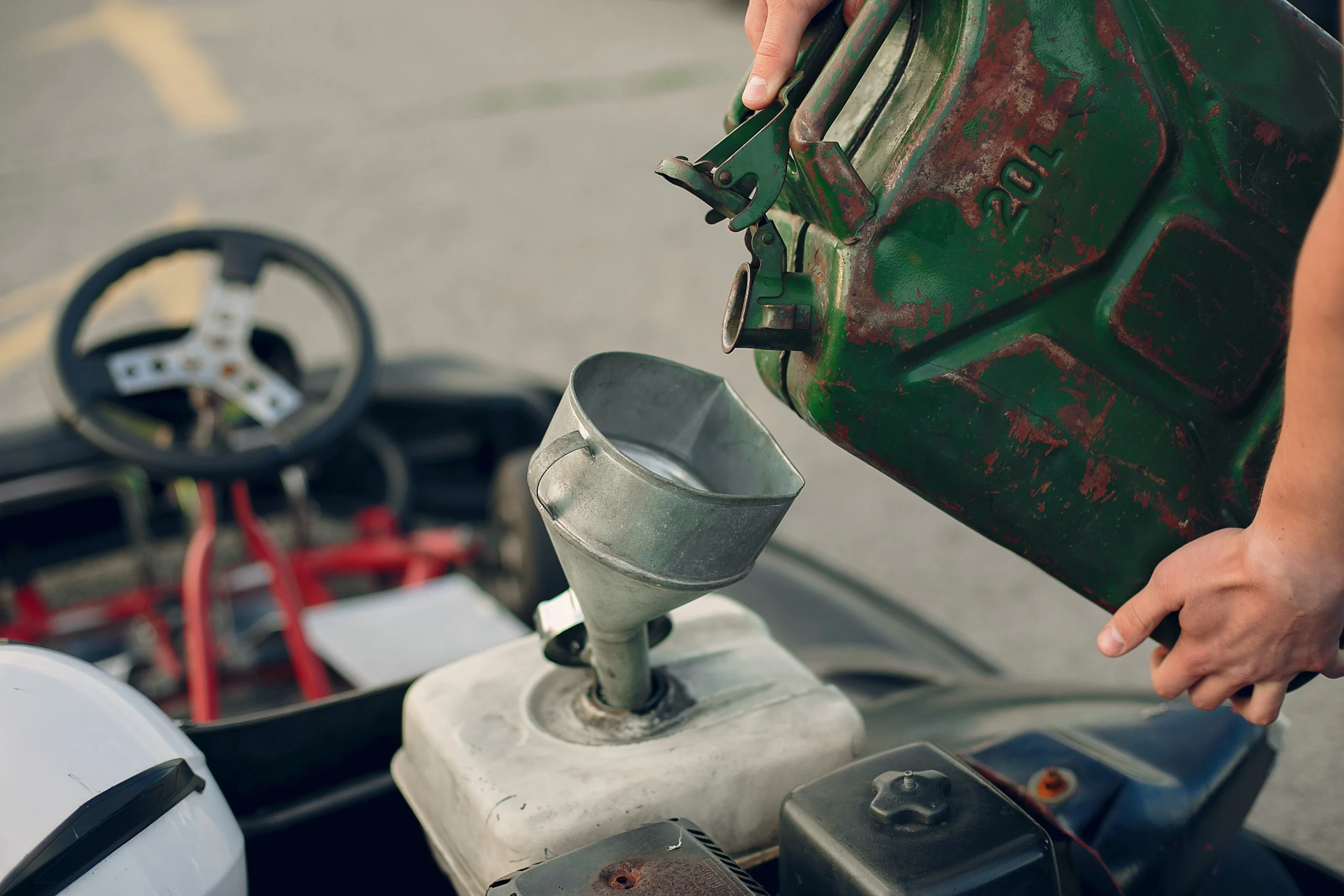 Worker pouring fuel into construction equipment fuel tank using a metal jerry can and funnel during outdoor refueling process