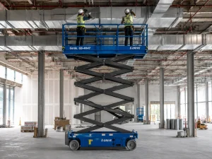Electric scissor lift with workers installing overhead services inside construction building